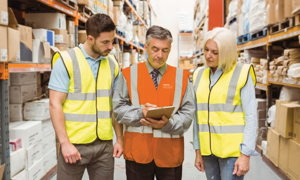 Instructor teaching two students wearing safety vests in warehouse