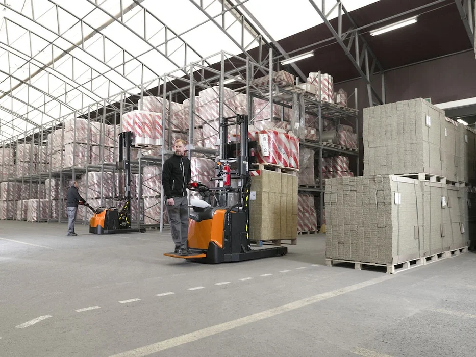 BT Staxio SPE120XRD, electric stacker with reach mast, double load handling, platform, and side guards. Application photo in warehouse environment.