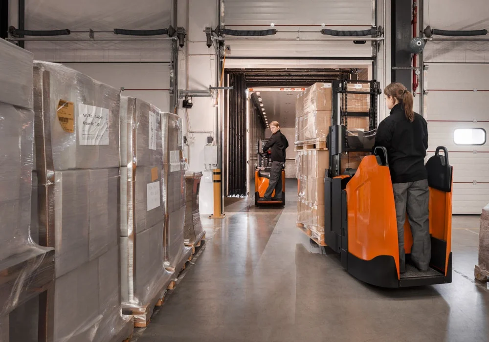 BT Staxio SPE200D, electric stacker with double load handling, platform, and fixed side guards. Application photo in loading bay.