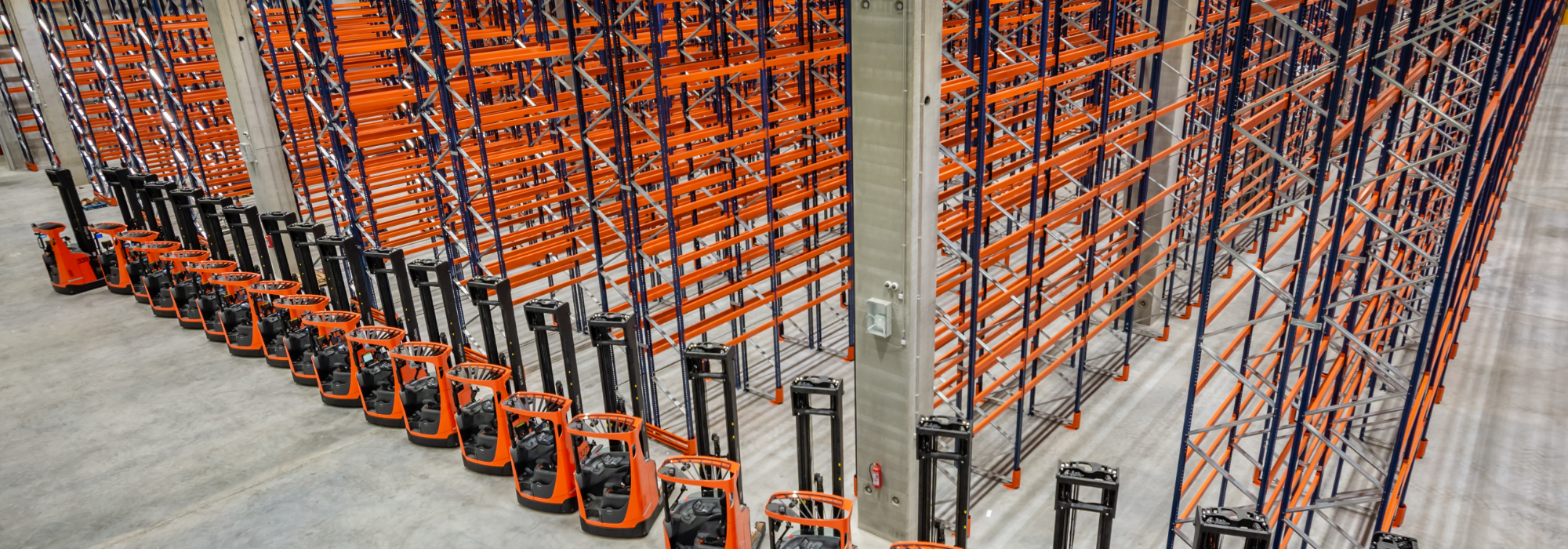 Photo of big warehouse with reach trucks lined up in front of high racking rows. 